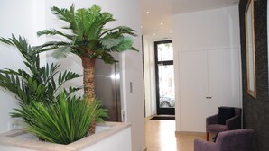 A modern hallway with a large potted palm tree, a purple armchair, and a view of a car through a glass door. - Lisbonne Appartements (Lisbon)