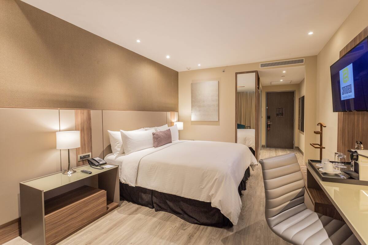 Une chambre d’hôtel moderne avec un grand lit, des tables de chevet, une télévision et un miroir.
