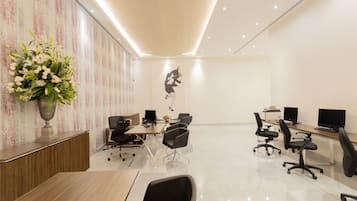 Un espacio de oficina moderno con un mostrador de recepción, varias estaciones de trabajo y una pared decorativa con un arreglo floral.