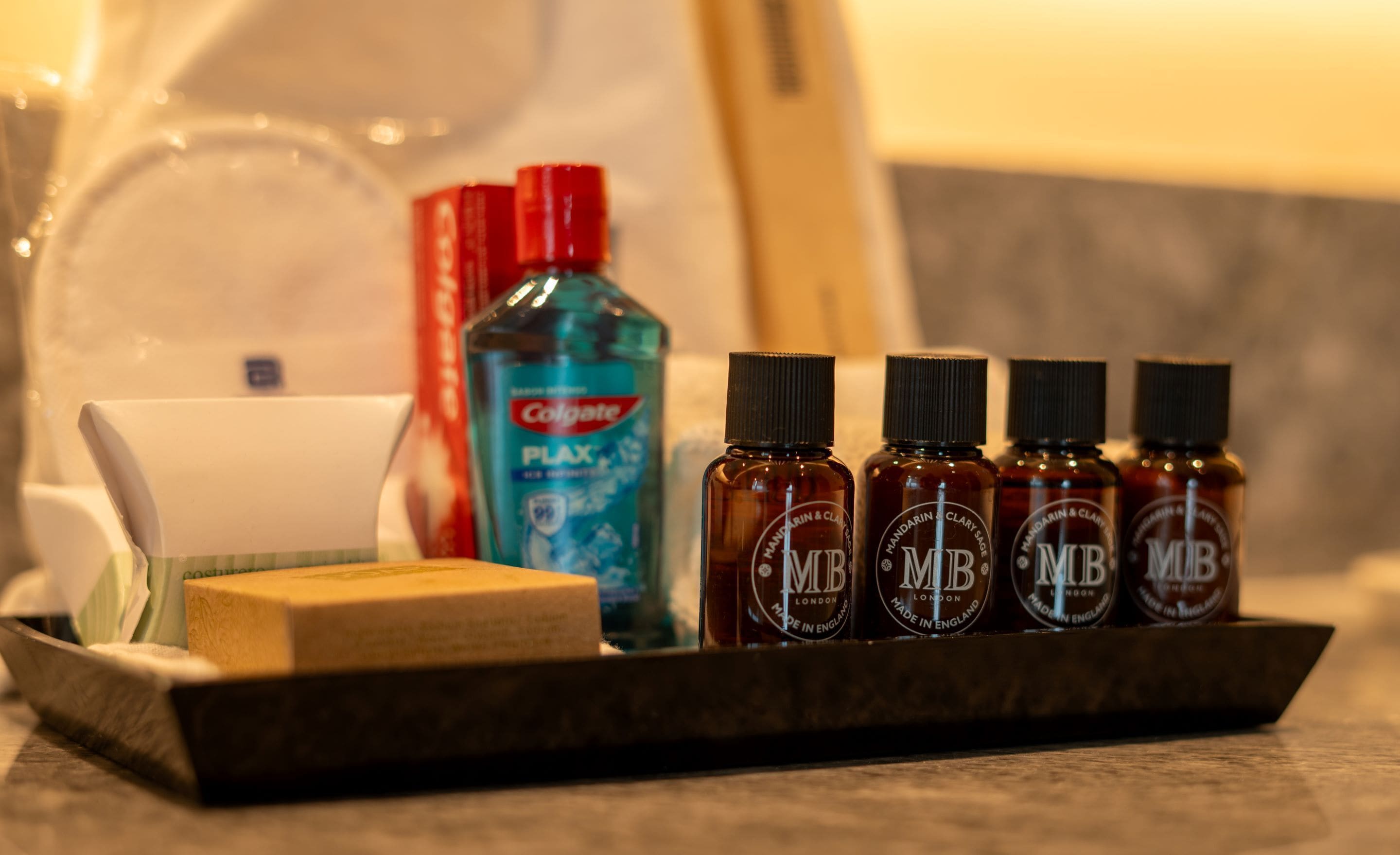 A tray with a bar of soap, a bottle of Colgate toothpaste, and four bottles of MR London essential oils.