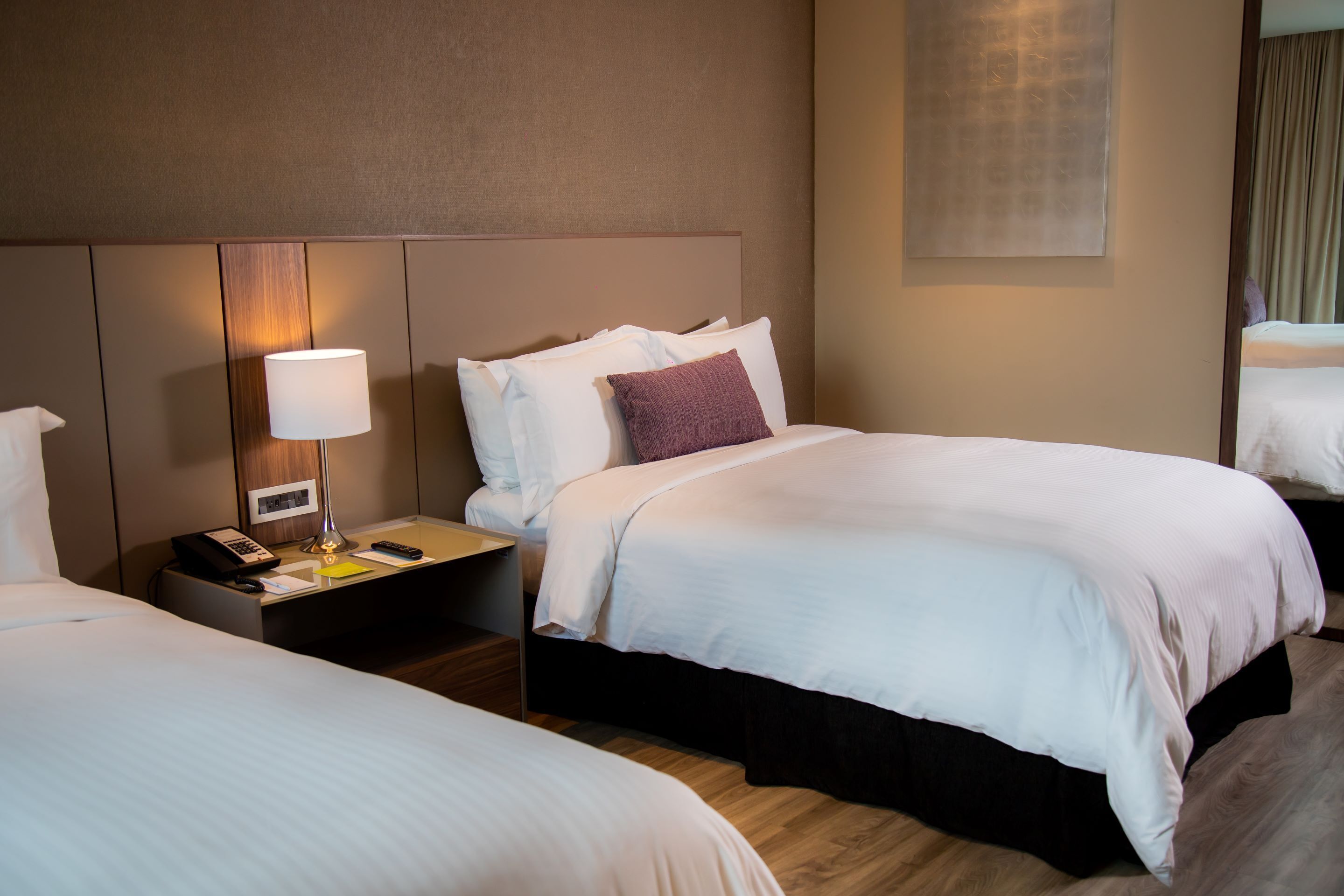 A hotel room with two beds, a nightstand with a lamp, a phone, and a framed picture.