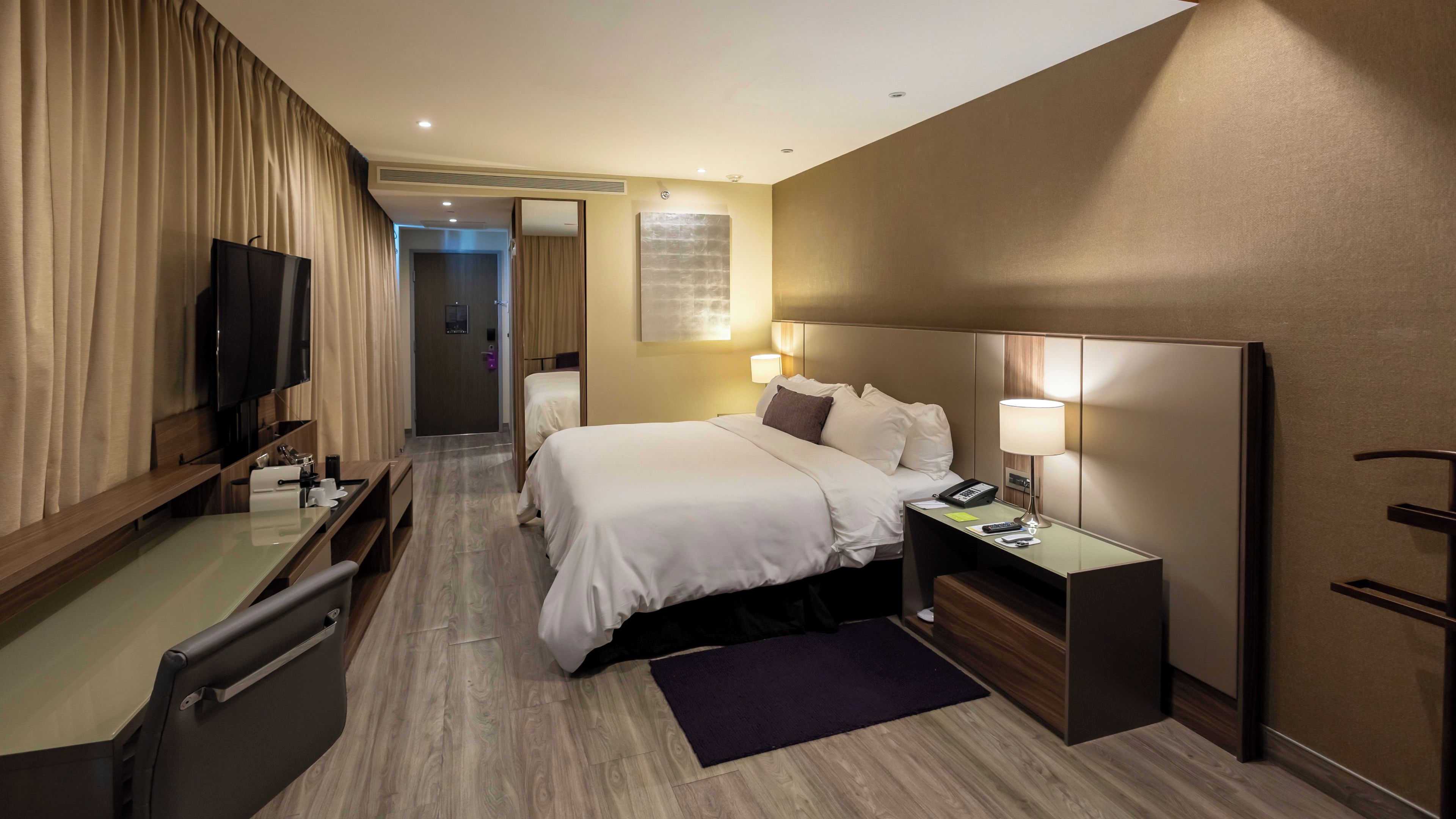 Camera d'albergo con un letto, comodino, lampada, televisione e una scrivania con una sedia.