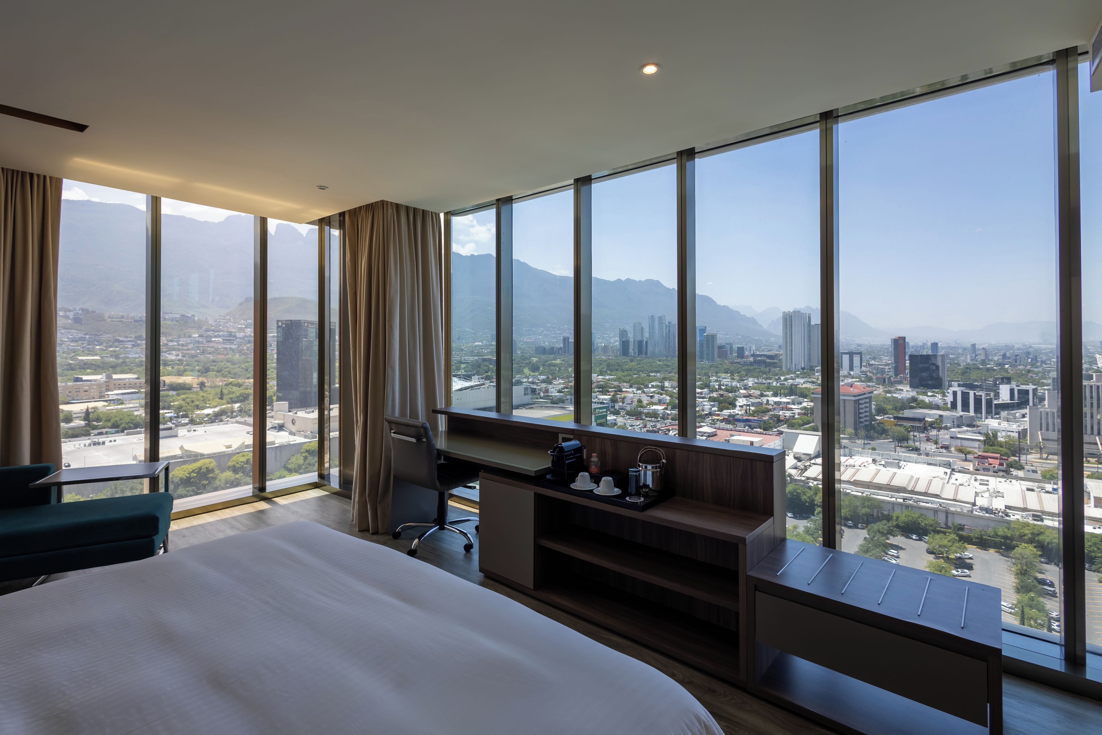 A hotel room with a large bed, a desk, and a view of a cityscape and mountains.