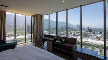 A hotel room with a large bed, a desk, and a view of a cityscape and mountains.