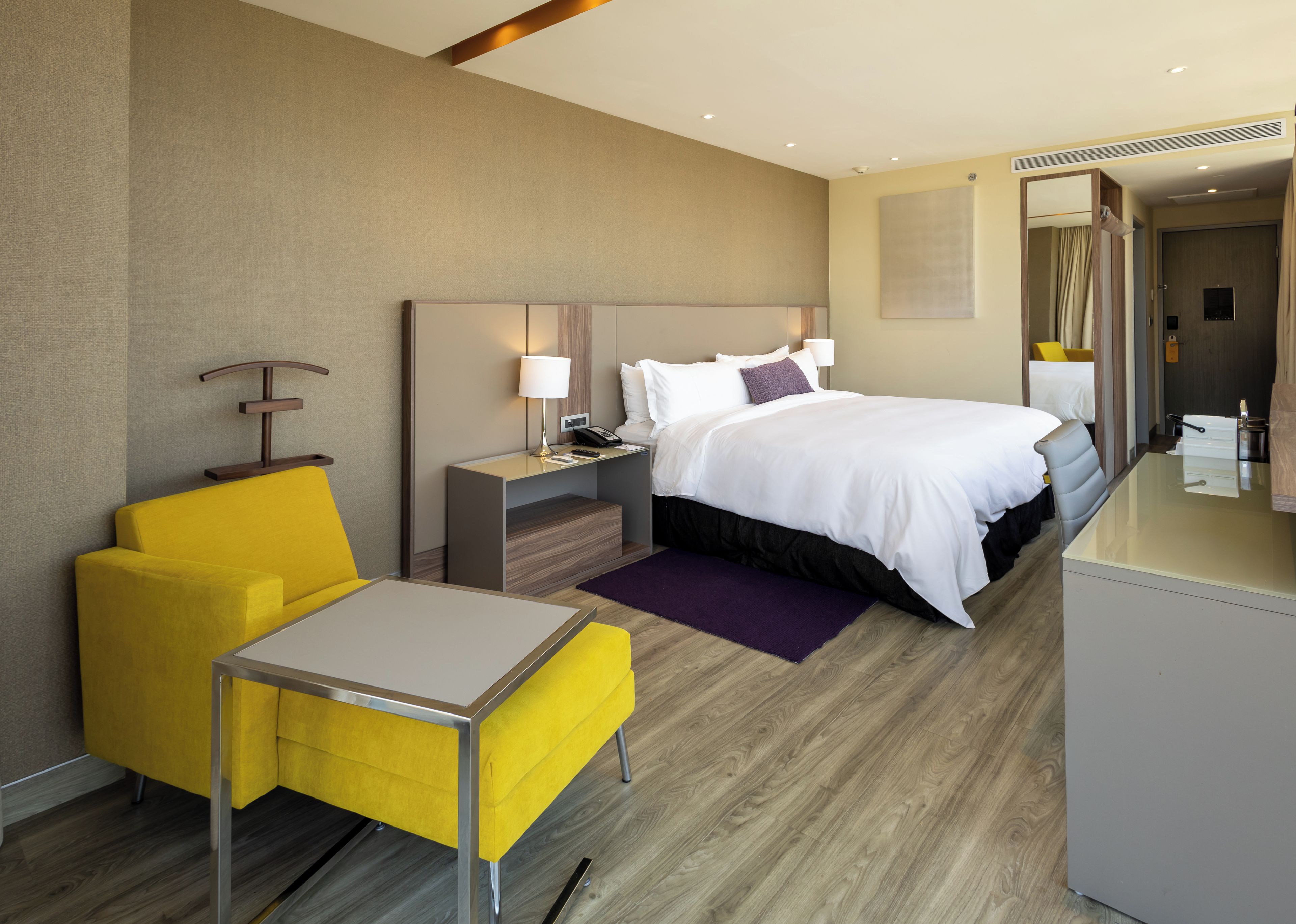 A hotel room with a bed, bedside table, lamp, chair, and a small table.