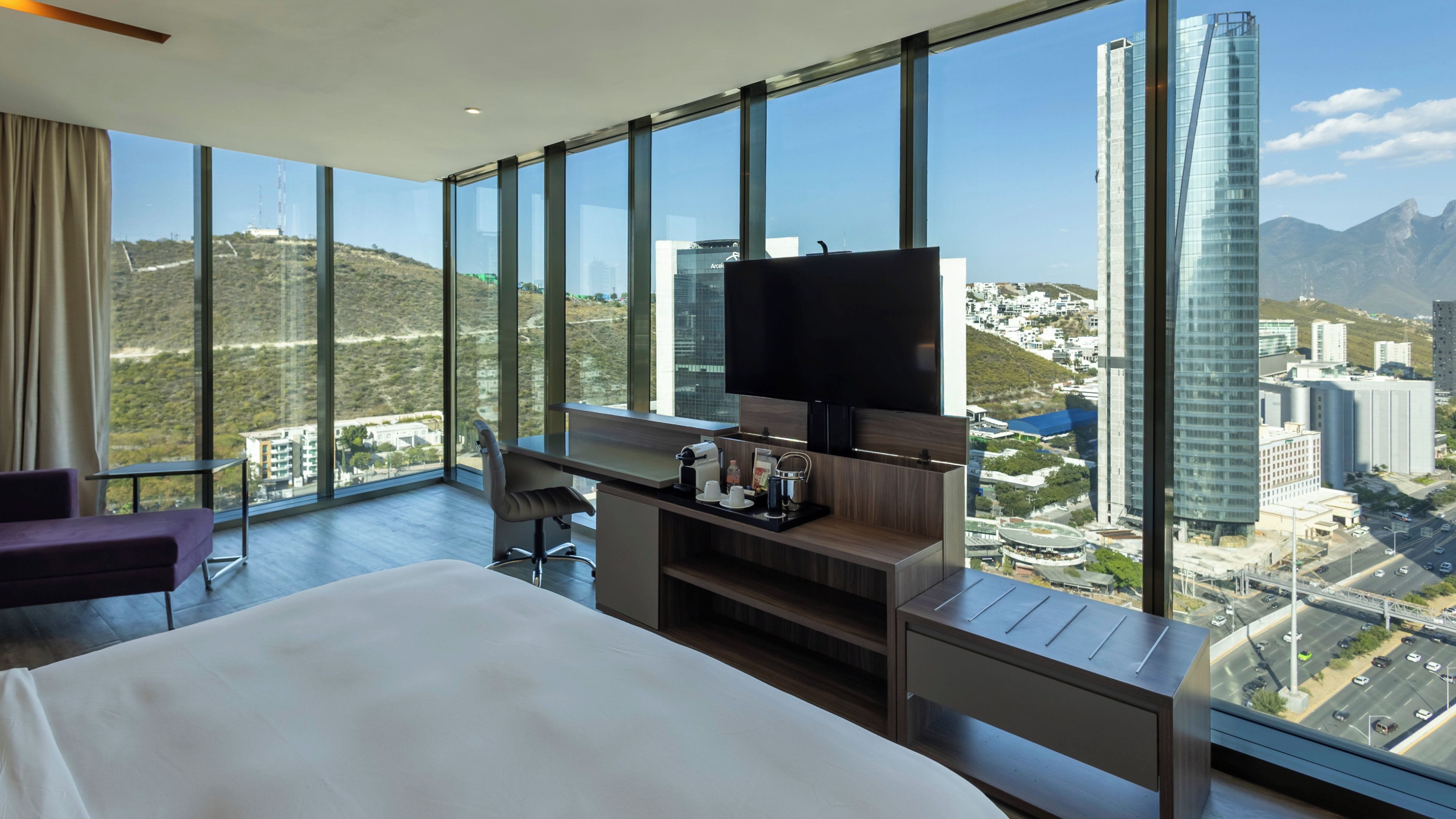 Hotelkamer met een groot bed, een bureau met een flatscreen televisie en een uitzicht op een stadsgezicht door grote ramen.
