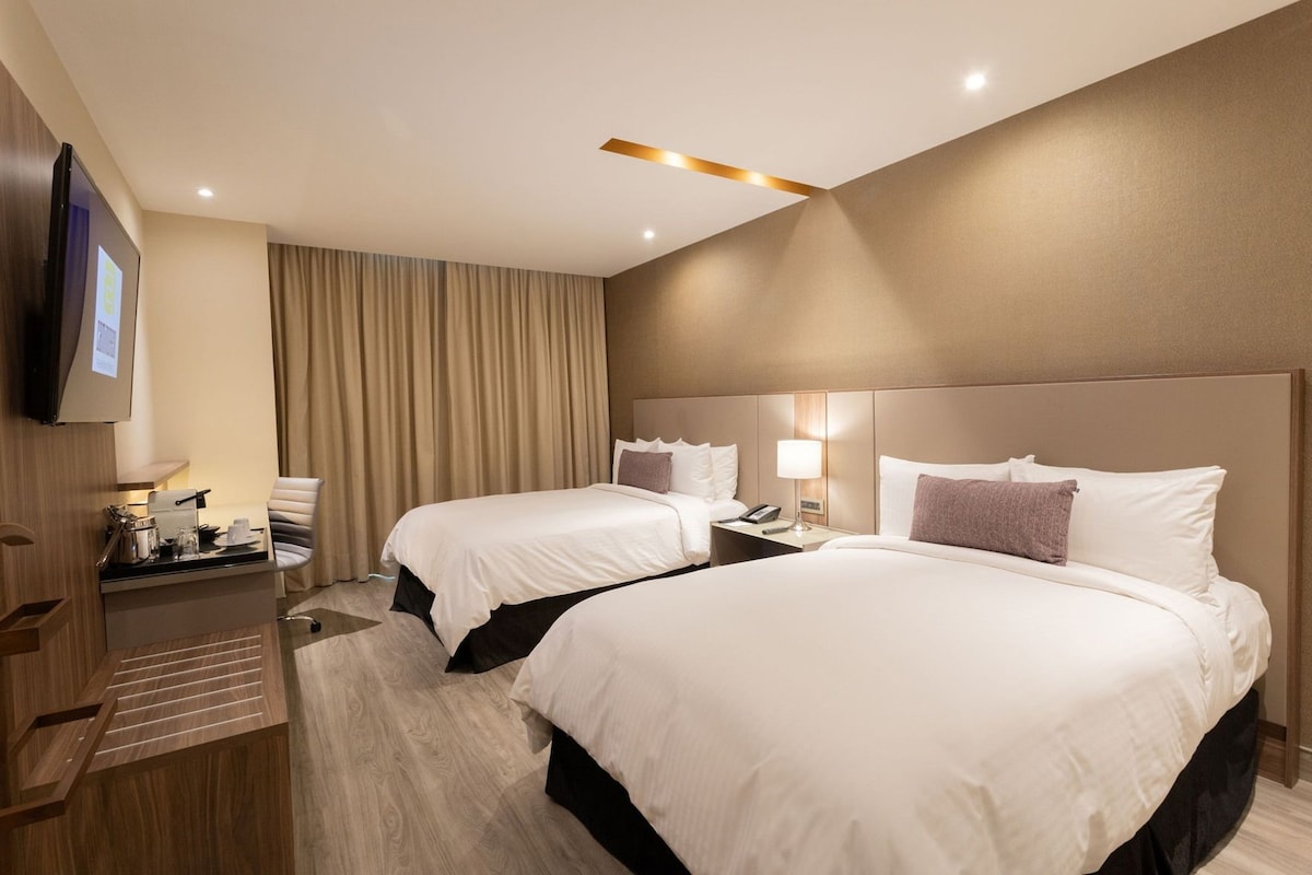 A hotel room with two beds, a desk, a chair, a TV, and a curtain.