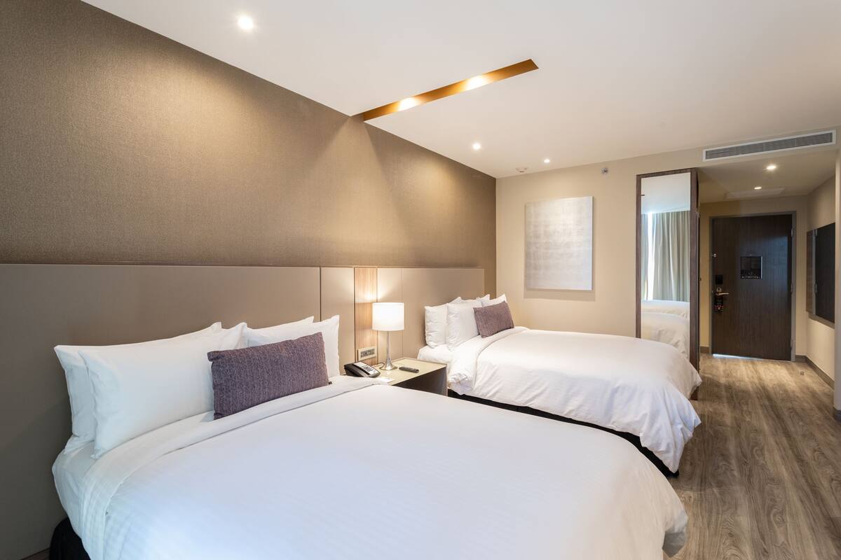 Une chambre d’hôtel avec deux lits, une table de chevet avec une lampe et une porte donnant sur une autre pièce.