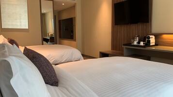 A hotel room with two beds, a TV mounted on the wall, a small table with a coffee maker, and a mirror.