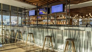 Uma área de bar com vários banquetes, um balcão repleto de garrafas e duas telas exibindo conteúdo.
