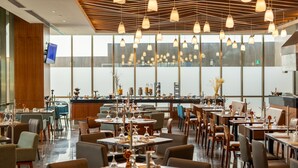 Um restaurante moderno com várias mesas e cadeiras, teto de madeira e iluminação pendente.