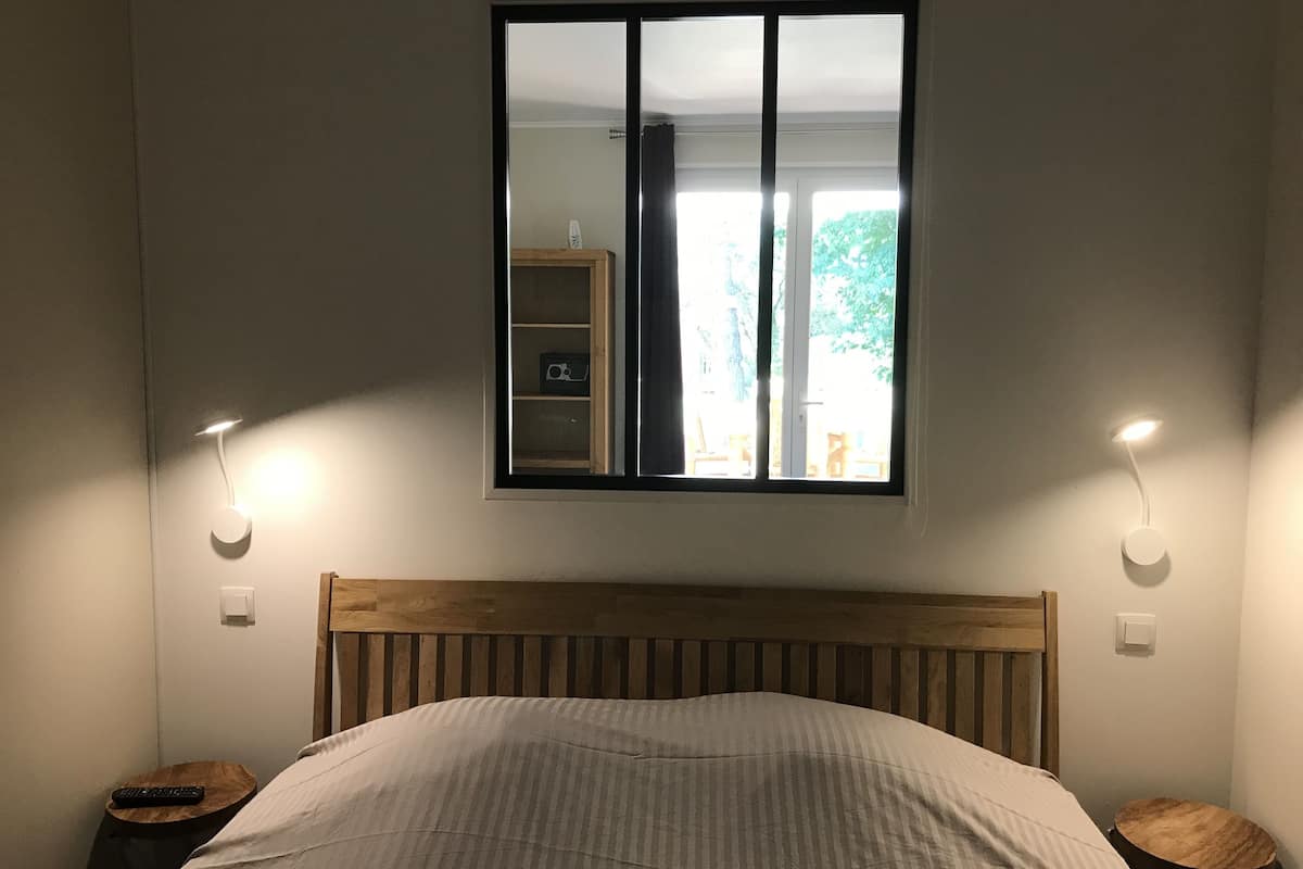 Ein Schlafzimmer mit einem Holz-Kopfteil, einem Bett mit gestreifter Bettdecke, zwei Nachttischen mit Lampen und einem Fenster mit Blick ins Freie.