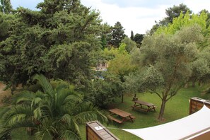 A backyard with a hammock, picnic table, and a small cabin-like structure surrounded by dense trees and greenery. - Résidence les Caraibes (Sérignan)