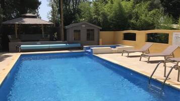A rectangular swimming pool with a tiled edge, surrounded by lounge chairs and a small building with a sloped roof.