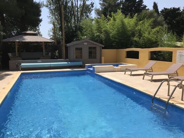 A rectangular swimming pool with a tiled edge, surrounded by lounge chairs and a small building with a sloped roof. - Résidence les Caraibes (Sérignan)
