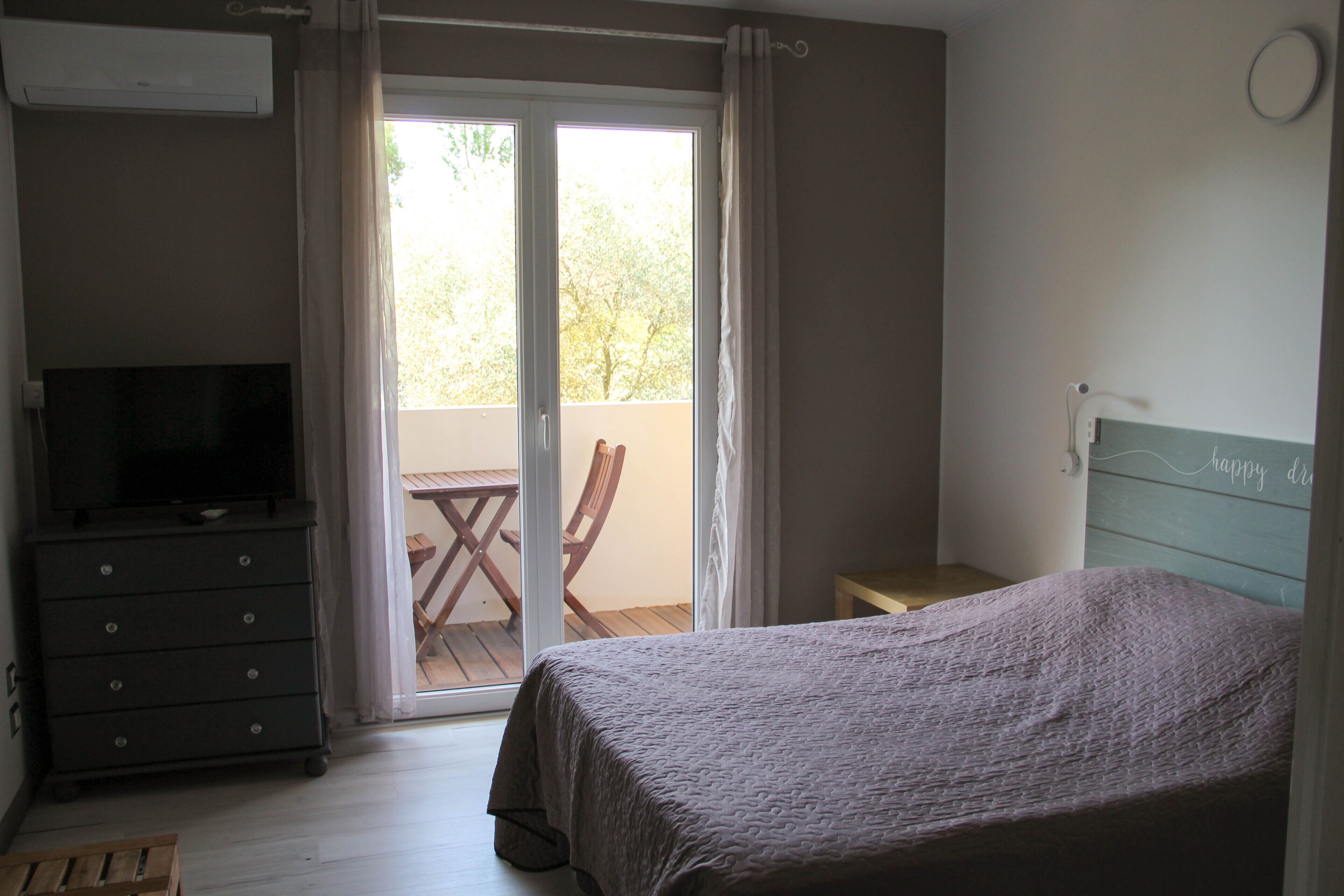 A bedroom with a bed, a dresser, a television, and a balcony with a table and chairs.