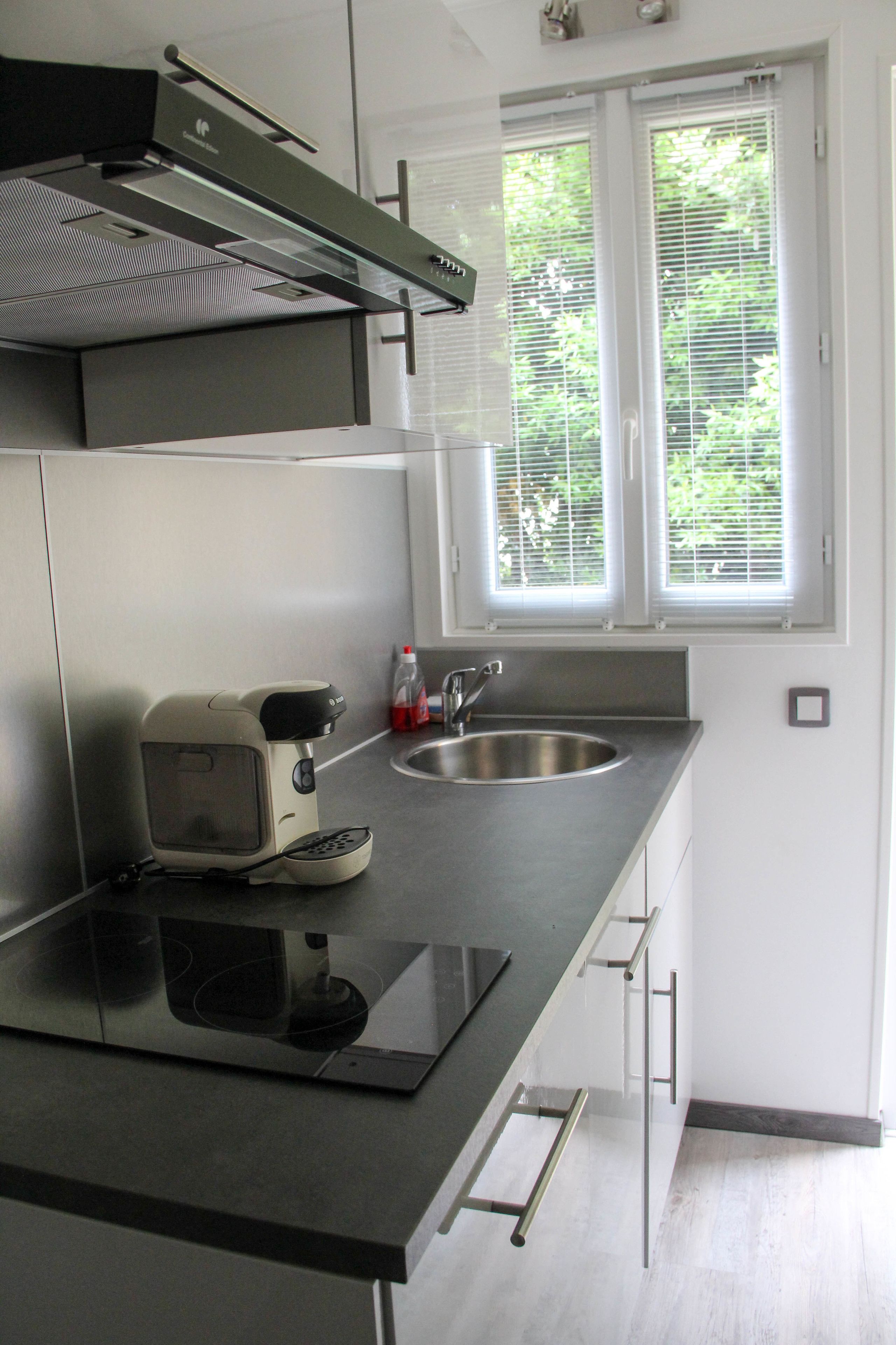 A modern kitchen with a built-in stove, a coffee maker, and a window with blinds.
