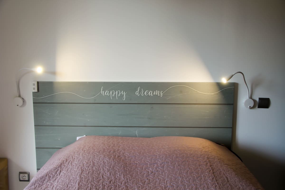 Ein Bett mit Kopfteil, auf dem "happy dreams" steht, beleuchtet von an der Wand montierten Lampen.
