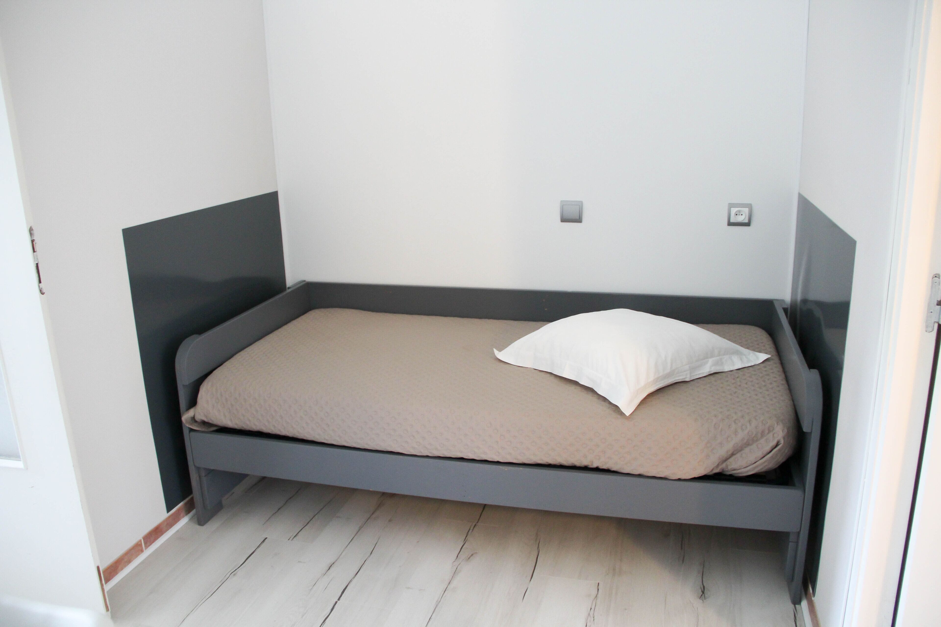 Habitació petita amb un llit individual, un marc gris i un matalàs beix.