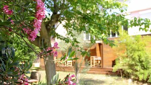 A wooden cabin with a deck and a garden with pink flowers. - Résidence les Caraibes (Sérignan)