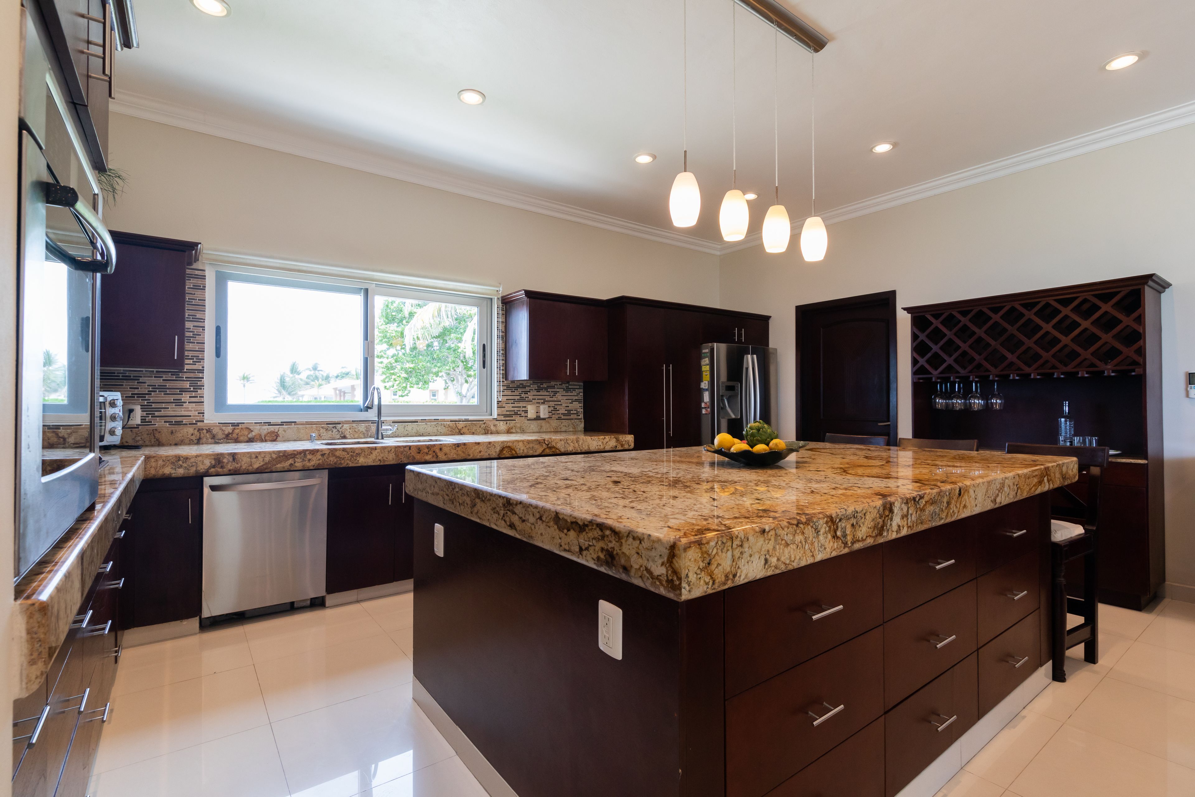 A modern kitchen with dark cabinetry, granite countertops, stainless steel appliances, and pendant lighting.