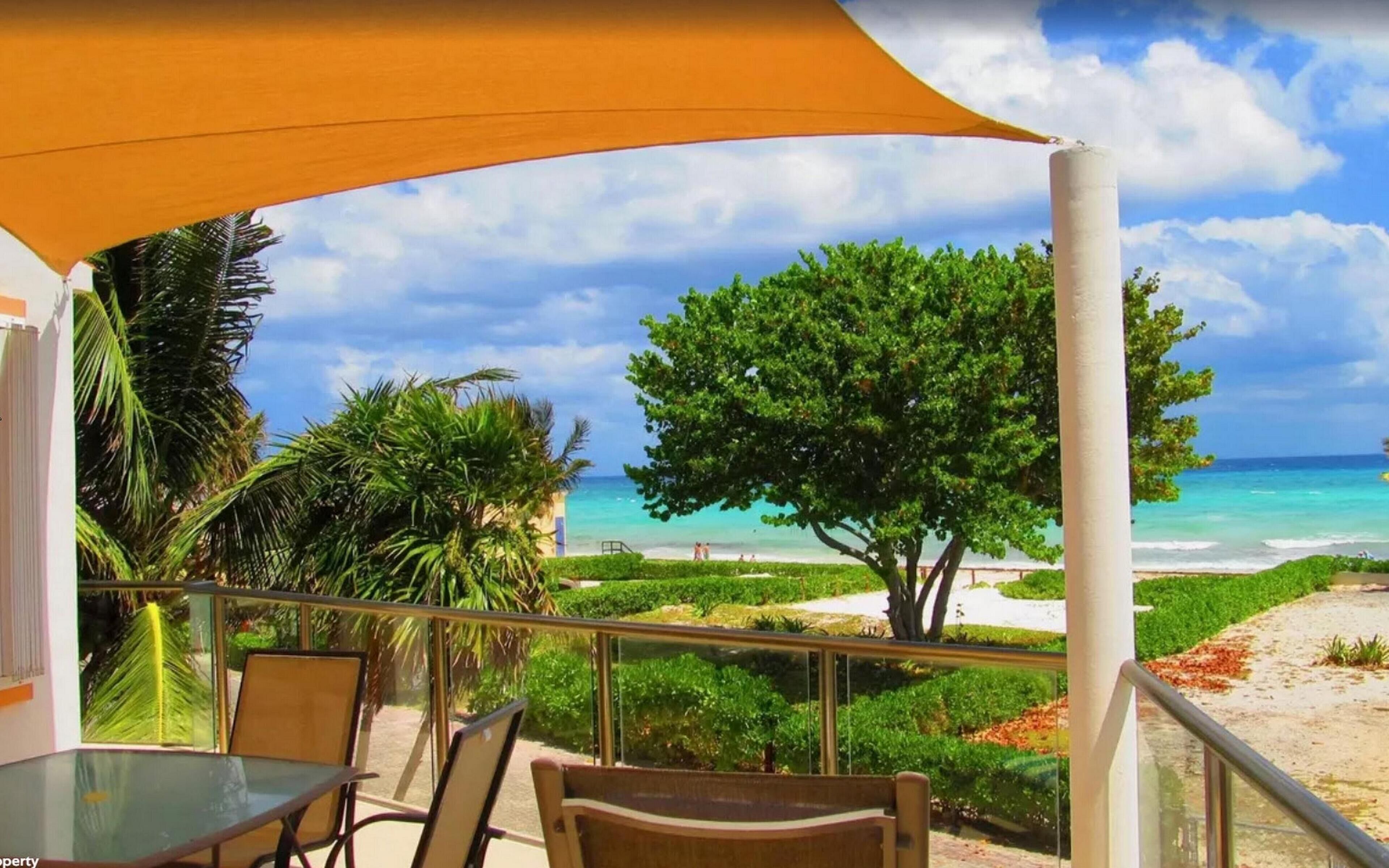 Ein Balkon mit Blick auf Strand und Meer, ausgestattet mit Tisch, Stühlen, einer Palme und einer weißen Säule.