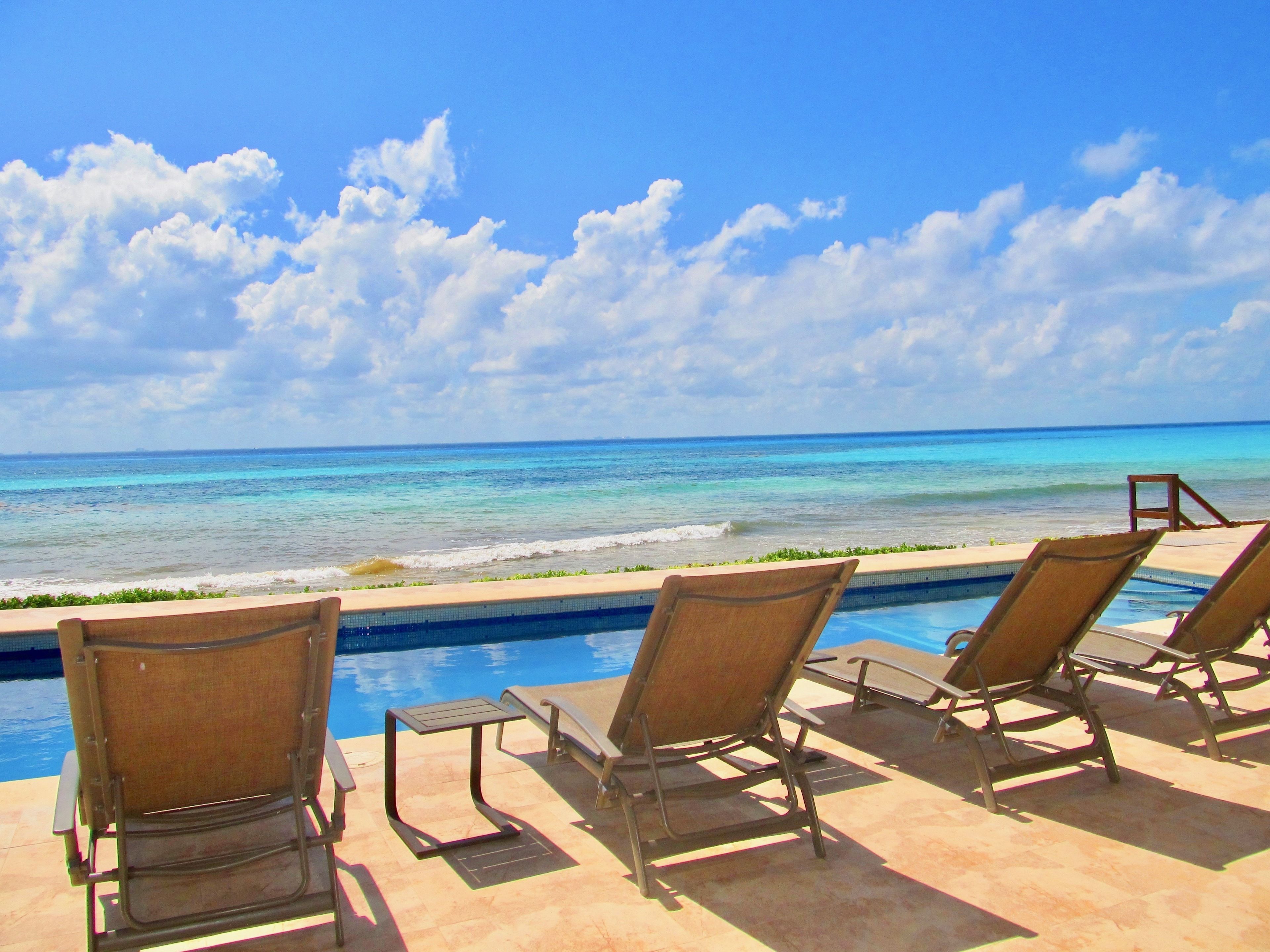 A poolside area with lounge chairs facing the ocean, a small pool, and a clear view of the sea.
