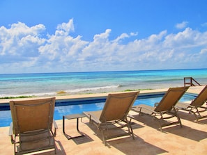 A poolside area with lounge chairs facing the ocean, a small pool, and a clear view of the sea.