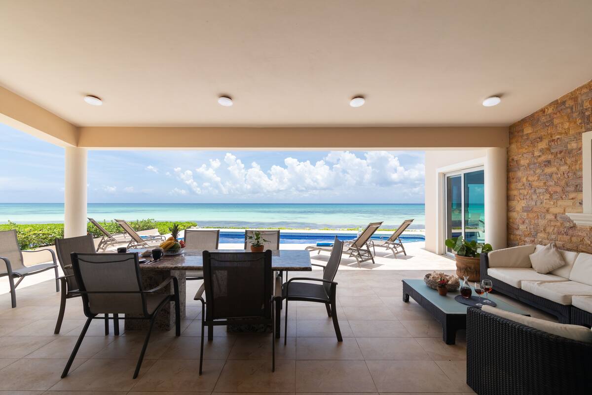 Un vaste espace extérieur comprenant une table à manger, des chaises et un canapé, avec vue sur une plage et l’océan.
