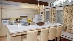 A kitchen with a central island, white cabinets, a microwave, a stove, and a refrigerator. There are four bar stools around the island. - 385 Forest Rd. 4 Bedroom Home by RedAwning (Vail)
