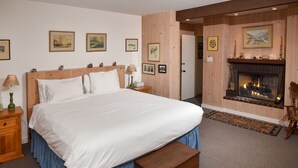 A large bed with a wooden headboard, a bedside table with a lamp, and a bench. There is a fireplace with a mantel and framed pictures above it. - 385 Forest Rd. 4 Bedroom Home by RedAwning (Vail)
