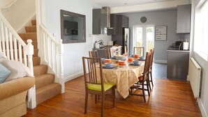 A dining area with a wooden table set for four, surrounded by wooden chairs. A staircase with white railings leads to another level. - Thomas Deluxe Bungalow (London)