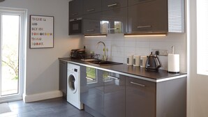 A modern kitchen with stainless steel appliances, a built-in washing machine, and a large window providing natural light. - Thomas Deluxe Bungalow (London)