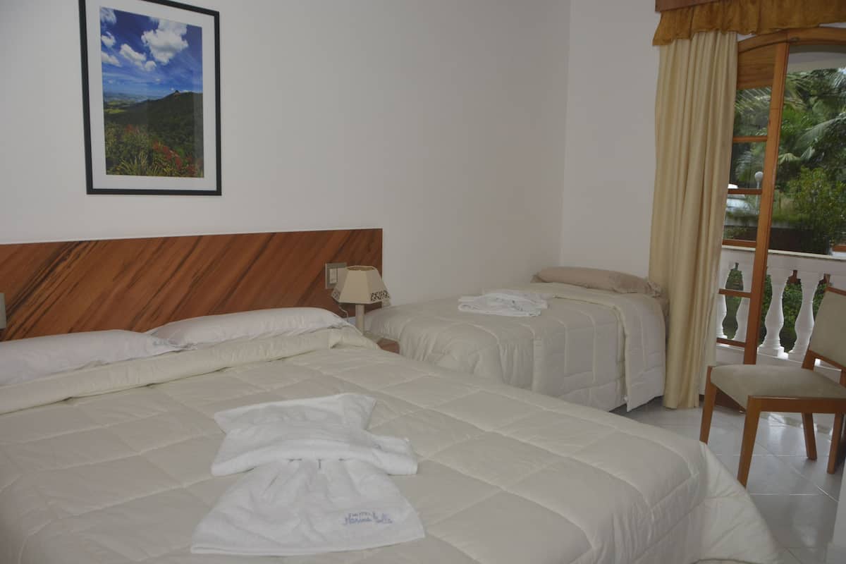 Habitación de hotel con dos camas, cabecero de madera, mesita de noche, lámpara, una silla y una ventana con cortinas.