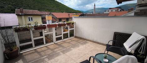 A balcony with potted plants, a table with a chair, and a view of a mountain and buildings.