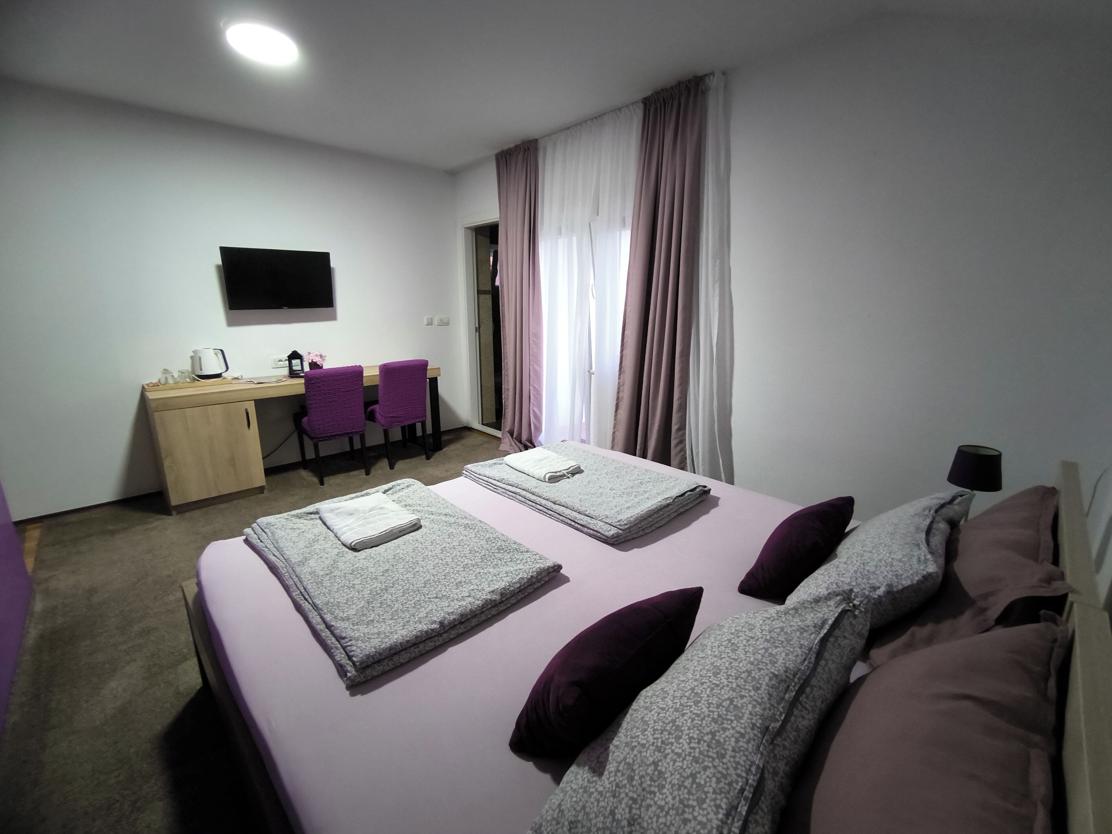 A hotel room with two beds, a desk, two chairs, a television, and a window with curtains.