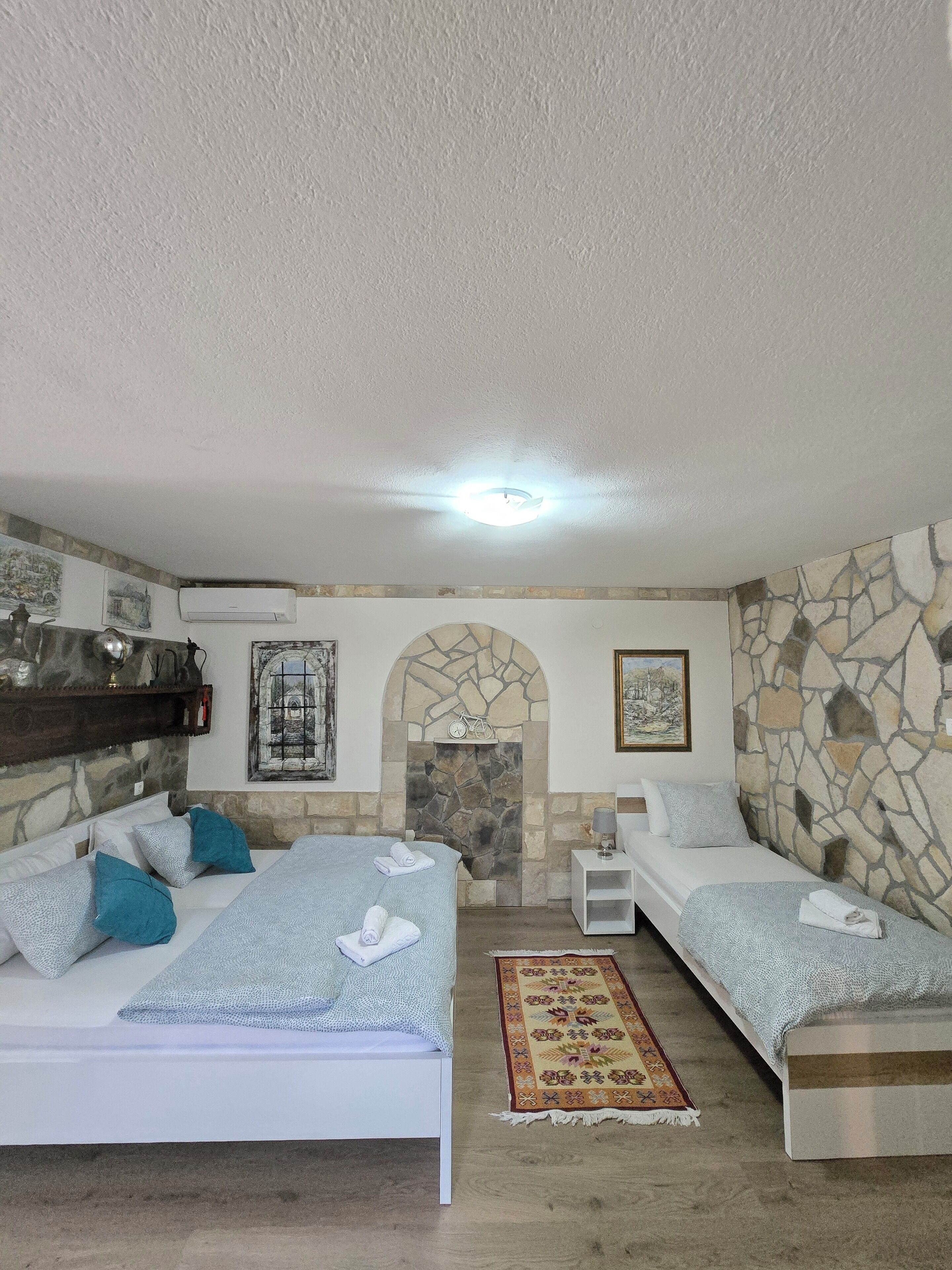 A bedroom with two beds, a stone fireplace, and a small table with a lamp.