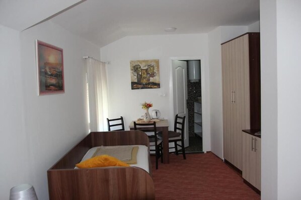 A small room with a bed, a table with chairs, a painting, and a wardrobe.