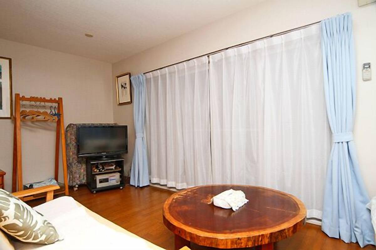 A living room with a wooden coffee table, a television on a stand, and a large window with curtains.