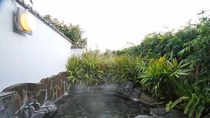 Un área de aguas termales con un muro de piedra, una fuente de agua y vegetación circundante.