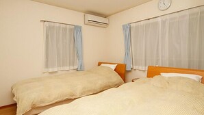 Habitación con dos camas, un reloj, aire acondicionado y cortinas translúcidas.
