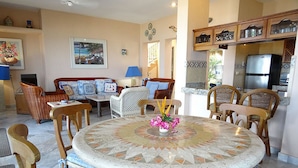 Un'area pranzo con un tavolo in mosaico, sedie in vimini e una cucina sullo sfondo.