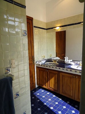 A bathroom with a tiled floor, a sink with a decorative mirror, and wooden cabinets.