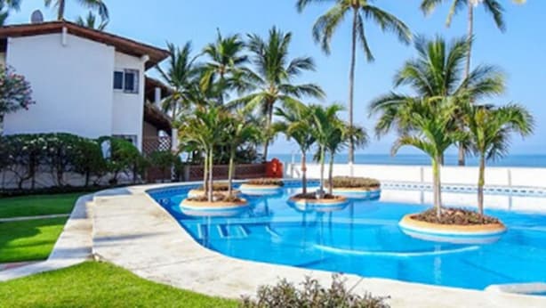 Un resort con area piscina, palme e un edificio con facciata bianca e tetto rosso.
