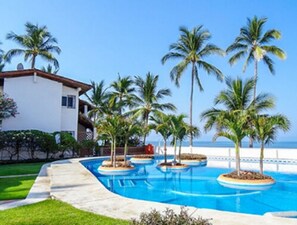 A resort with a pool area, palm trees, and a building with a white facade and red roof. - Casa Inglesa by Las Palmas (Bucerías)