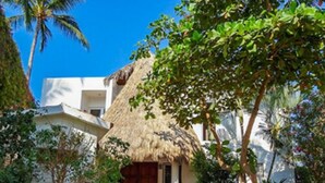 Un edificio bianco con tetto di paglia, circondato da vegetazione lussureggiante e palme.