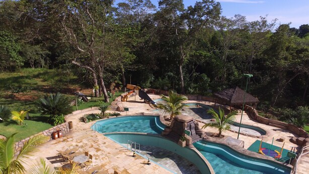 A swimming pool with a tropical theme, surrounded by palm trees and a thatched-roof structure. - Thermas do Bosque Lineacaldas (Caldas Novas)