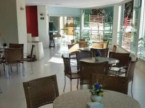 A dining area with round tables and chairs, a central flower arrangement, and large windows with blinds. - Thermas do Bosque Lineacaldas (Caldas Novas)