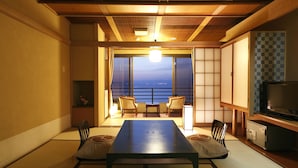 A traditional Japanese room with tatami flooring, a low table, chairs, a television, and a view of the sea. - Aoki-nagi-no-yado Meijikan (Izu)