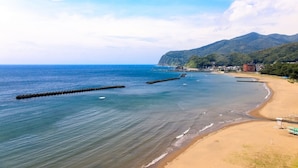 A coastal beach with a clear view of the ocean, a sandy shore, and a mountain range in the background. - Aoki-nagi-no-yado Meijikan (Izu)